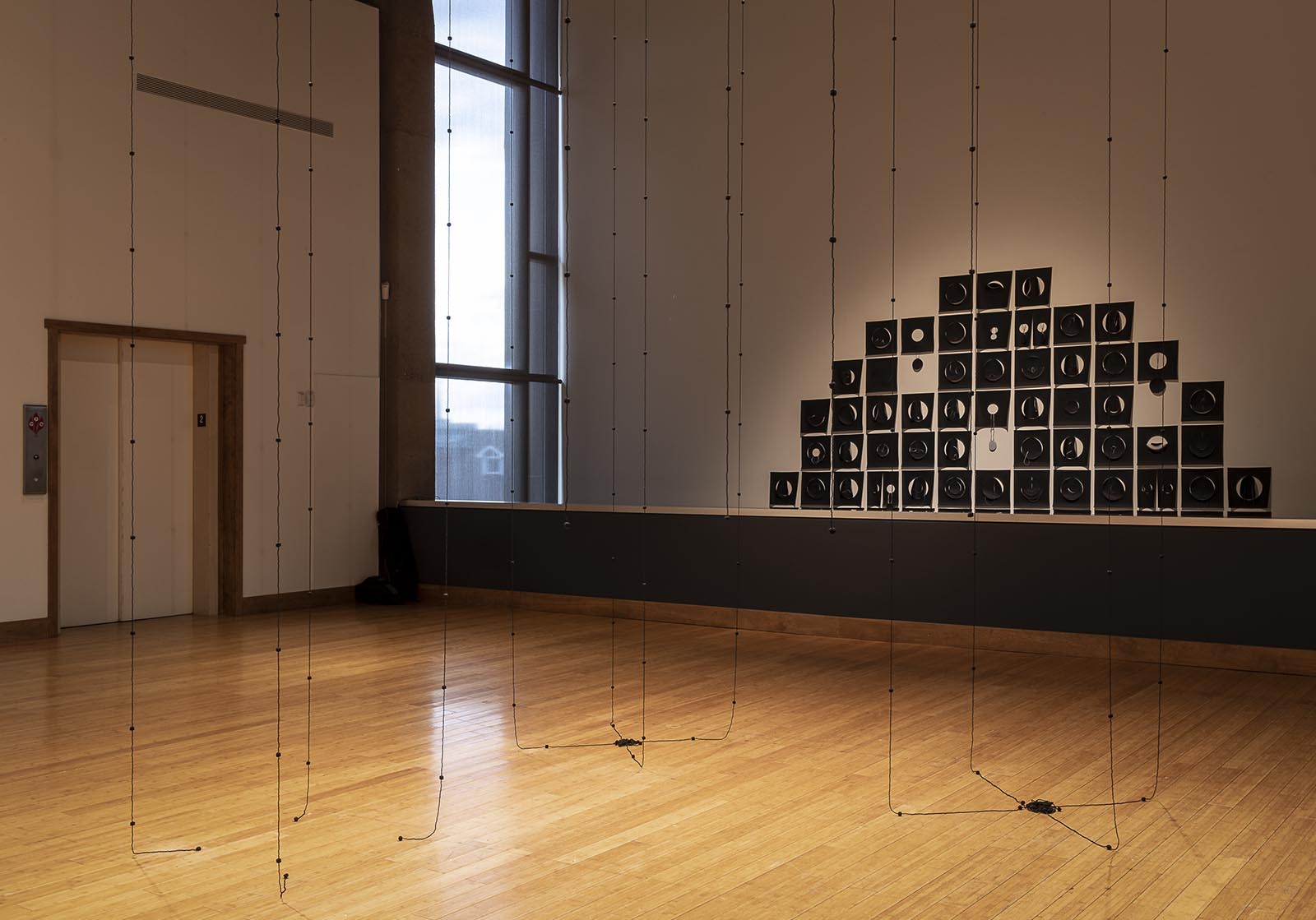 Installation view of "Within/Without". 2022. Glass beads, nylon thread. Installed from within drop ceiling. Seen here with "Squaring Circles" in the background.